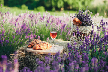 A glass of wine, two croissants and a wicker basket with baguette and a bouquet of lavender inside...