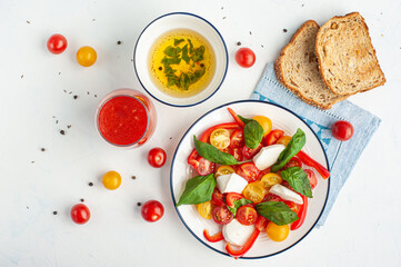 A light summer dinner. Red and yellow vegetable salad, tomato juice, basil sauce and toast.