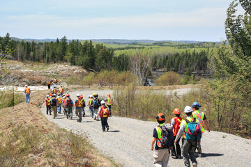 SUDBURY, ONTARIO, CANADA - MAY 21 2009: Group of workers and geologists in hardhats and high-visibility vests walking on road to geological outcrop site.