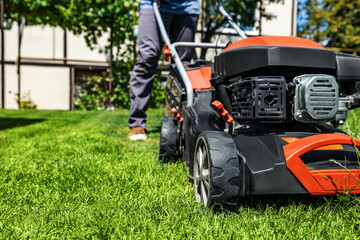A man moves with a lawn mower and mows green grass. Garden care concept
