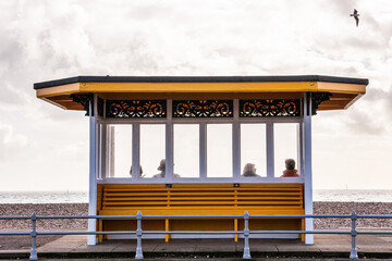 elderly people sat inside a Victorian shelter or on a bench at the seaside in winter