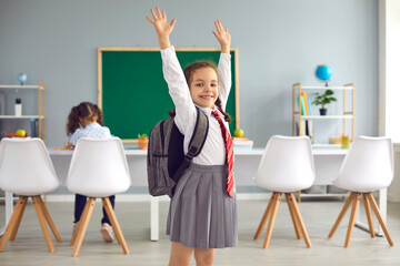 Concept back to school. Happy schoolgirl smiling raised her hands up while standing in class.