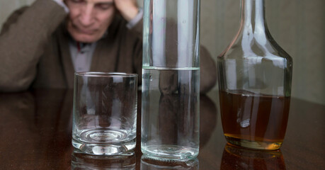 disappointed old man holds hands on head sitting at brown wooden table with bottles
