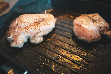 Juicy chicken being fried on a hot steamy black griddle in oil