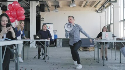 A young office employee takes the horn and calls all his colleagues to dance. Managers have fun and dance together. Festive office atmosphere.