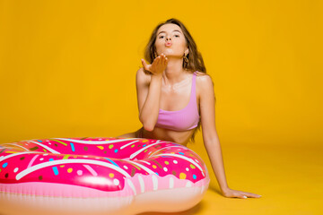 Obraz na płótnie Canvas Waiting for Vacation. Millennial Blonde Woman Sitting On Donut Inflatable Ring, Dreaming about Summer Time, yellow studio background