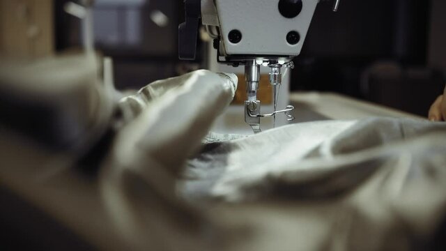Seamstress at the sewing machine sews light fabric closeup.
