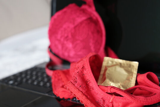 Female lace panties, red bra and condom on laptop, selective focus. Concept of sex after work, contraception, seductive lingerie