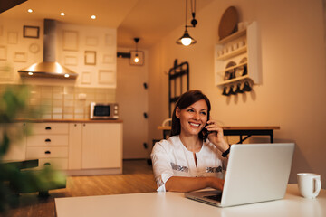 Smiling woman having phone call on mobile phone and using laptop at home, portrait.