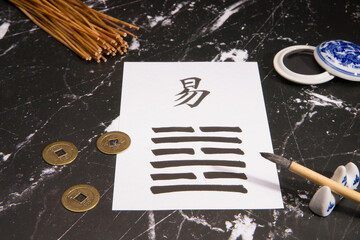 Close up of an I Ching arrangement with the 63th hexagram (After Completition/Chi Chi) written with a chinese ink brush on rice paper. There is also a chinese ink tank and three chinese coins.
