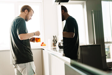 Photo of caucasian redhead man drinking tea while standing in kitchen