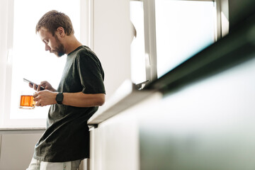 Photo of redhead man beard drinking tea while using mobile phone