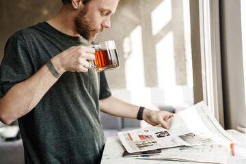 Photo of serious redhead man reading newspaper while drinking tea - Powered by Adobe