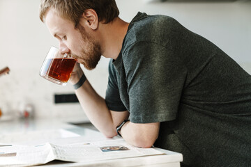 Photo of serious redhead man reading newspaper while drinking tea