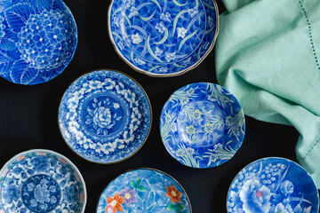 Blue and white decorative Japanese ceramic plates on black background - overhead photo