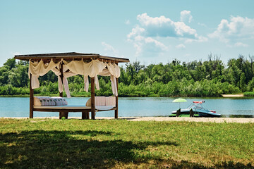 Weekend on vacation on a sandy beach. Gazebo with curtains on the river. Yacht is moored to berth...