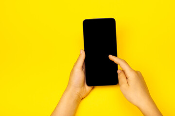 Smart phone in child's hands on the yellow backstage. The concept of necessary things of a little girl, technology for children. Flat lay, copy space.