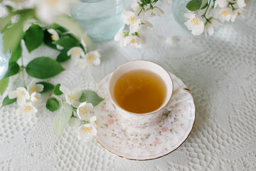 White blossom jasmine flowers in vase on the table with a cup of tea
