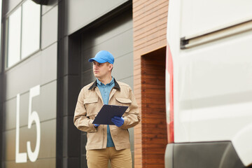 Young delivery person in uniform working with loads in warehouse outdoors