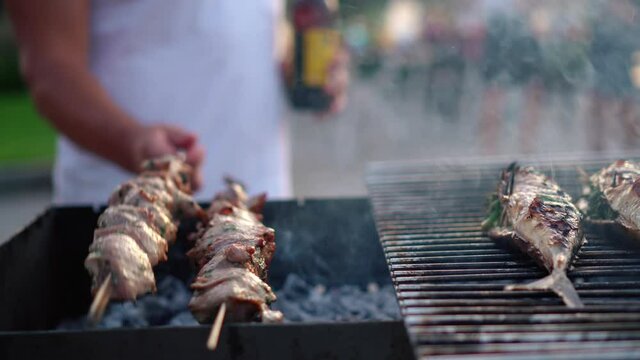 Man holding bottle upturn spit with pork meat. Smoke rising from grilled fish