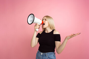Fototapeta na wymiar Shouting with megaphone. Portrait of young woman with bright emotions on coral pink studio background. Blonde female model. Concept of human emotions, facial expression, sales, advertising, youth.