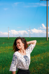 A young brunette woman with long hair stands in the background of a picturesque panorama with a green meadow, blue clouds and power lines, a place for copy space