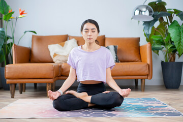beautiful asian-looking girl sitting on a carpet in a sports uniform at home in lotus position

