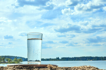 Obraz premium Clear fresh water in a glass against background of river or lake. Healthy food and environmentally friendly water.