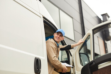 Naklejka premium Young smiling courier holding package while sitting in the van he delivering parcels