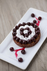 tasty chocolate iced cake with meringue and cherry served on white plate on a wooden table