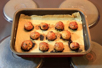 Baked small meatballs in a tray with baking paper at an oven top