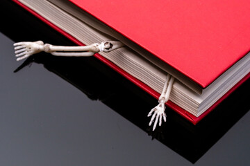parts of the human skeleton crawling out of a closed red book. horrible mystery books