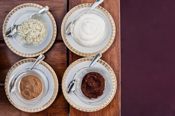 Overhead view of cinnamon powder, cocoa powder and cream in bowls on wooden table