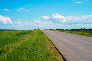 Highway in the middle of green picturesque fields against a blue sky with clouds.