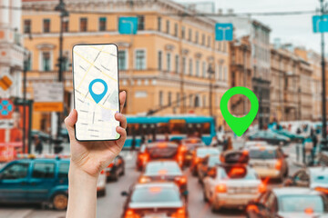 A female's hand holds a smartphone with an online map app. In the background is a city street with...