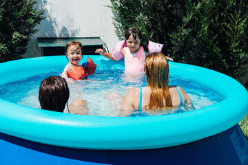 A couple of lesbian women bathe in the pool with their daughters wearing muffs in summer