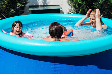 A couple of lesbian women bathe in the pool with their daughters wearing muffs in summer