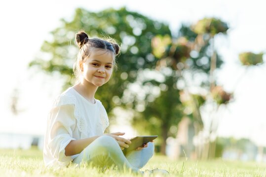 Child with tablet pc outdoors. Little girl on grass with computer
