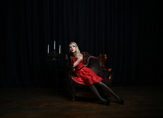Obraz na płótnie Canvas beautiful girl in a red dress posing in a chair on a black background