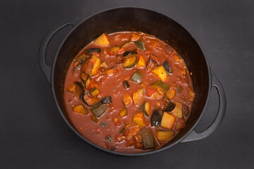 Vegetable ragout in a black Dutch oven photographed against a black background
