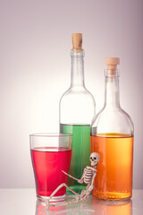 the skeleton is on the background of three bottles with various alcoholic drinks on a gray background