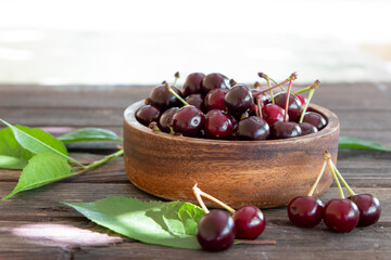 Fresh garden cherries in a wooden bowl on a vintage wooden background with copy space