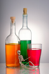 the skeleton is on the background of three bottles with various alcoholic drinks