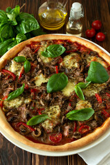 Delicious Italian pizza and cherry tomatoes and basil on brown wooden background. Copy space.