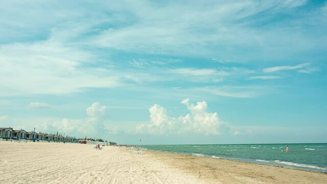 Clouds timelapse in blue summer sky. Sand beach with random peolpe having sunbath near Azov sea. Ukraine, Arabat Spit 2020.