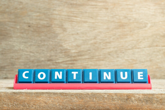 Tile letter on red rack in word continue on wood background
