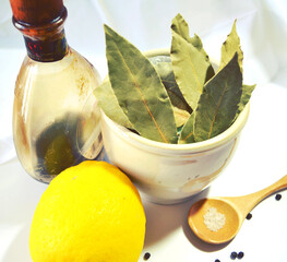 Food still life with bay (laurel) leaves in ceramic pot, lemon, sea salt in wooden spoon, pepper...