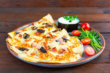 Delicious pancakes with mushrooms, ham and cheese, arugula, tomatoes and sour cream on a wooden background