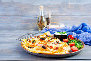Delicious pancakes with mushrooms, ham and cheese, arugula, tomatoes and sour cream on a wooden background