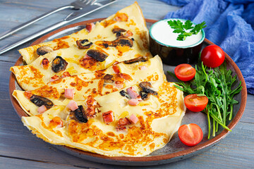Delicious pancakes with mushrooms, ham and cheese, arugula, tomatoes and sour cream on a wooden background